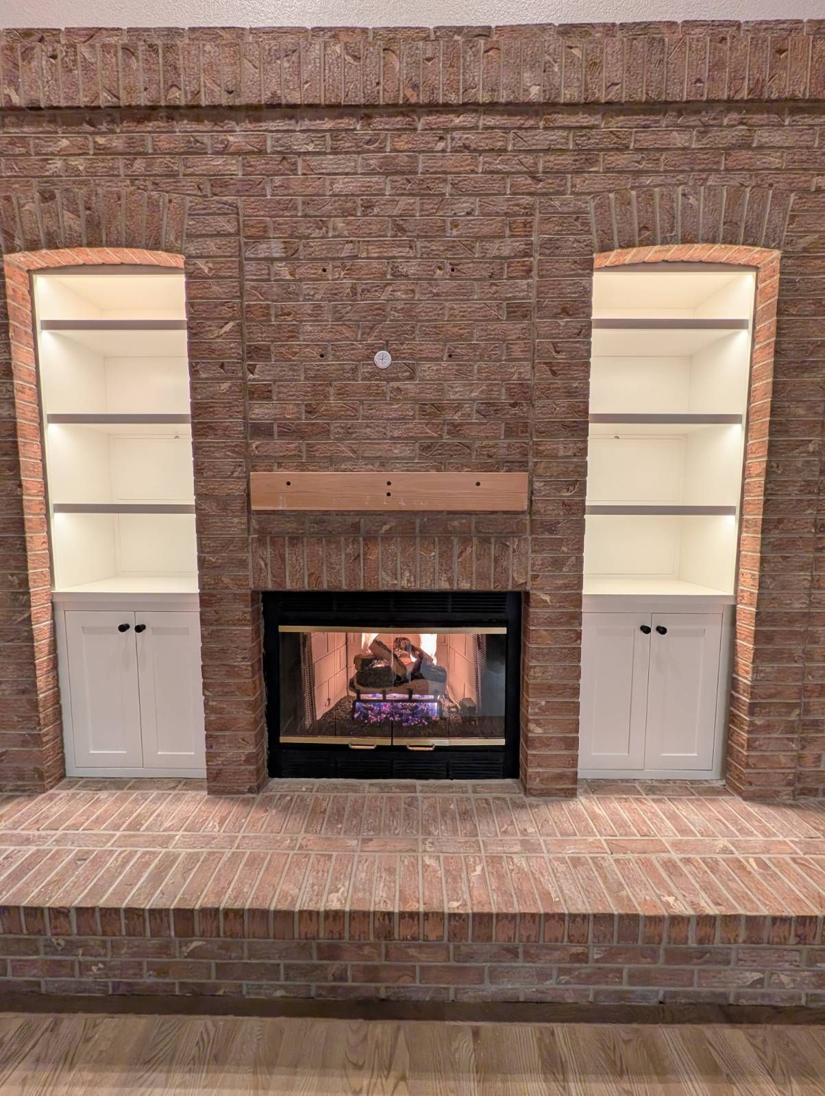 Brick fireplace with lit firebox, built-in shelves, and white cabinet doors on both sides
