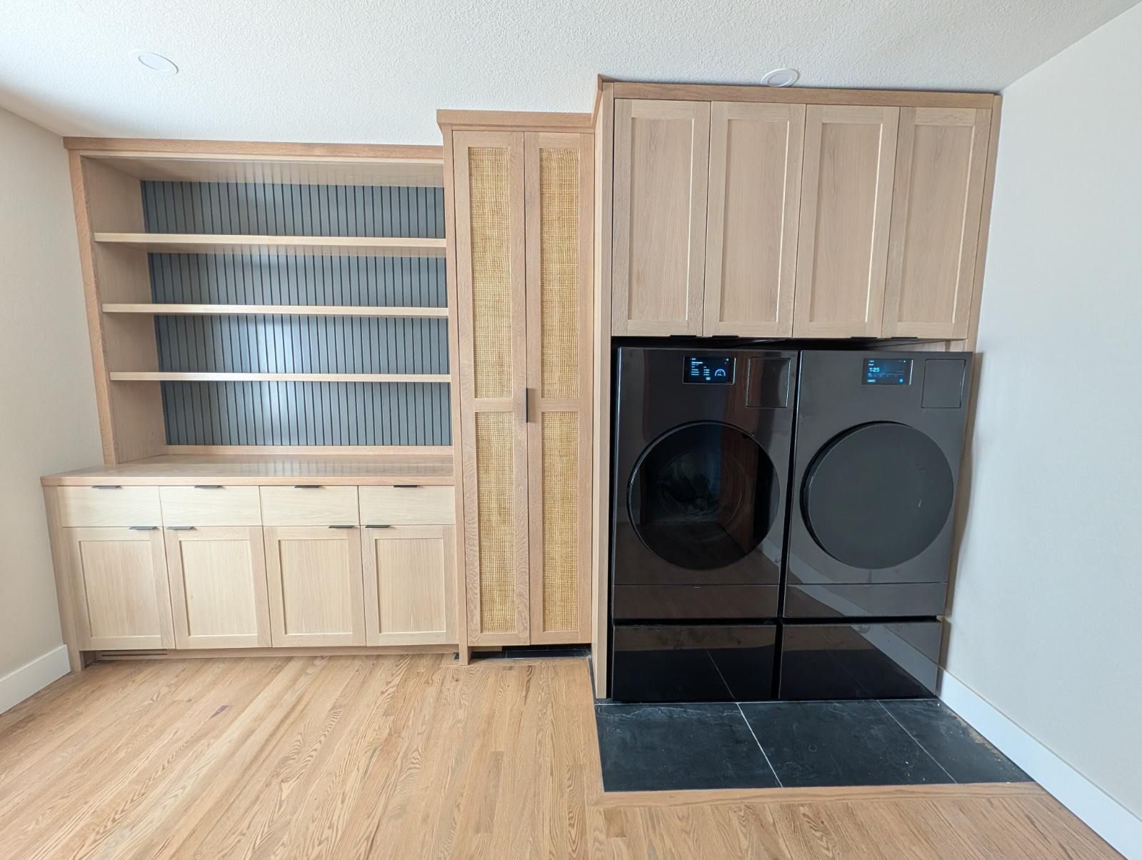 Laundry room with built-in shelves, cabinets, and a black front-loading washer and dryer.