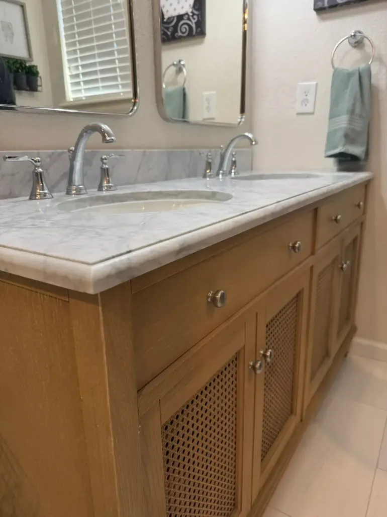 Bathroom vanity with marble countertop, silver faucet, and wood cabinets with woven panels