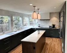 Modern kitchen with dark cabinets, white countertops, a wood island, and large windows overlooking trees