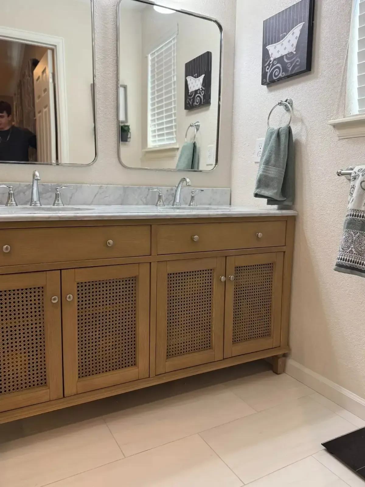 Bathroom vanity with double mirrors, wood cabinet, and towels on a beige wall.