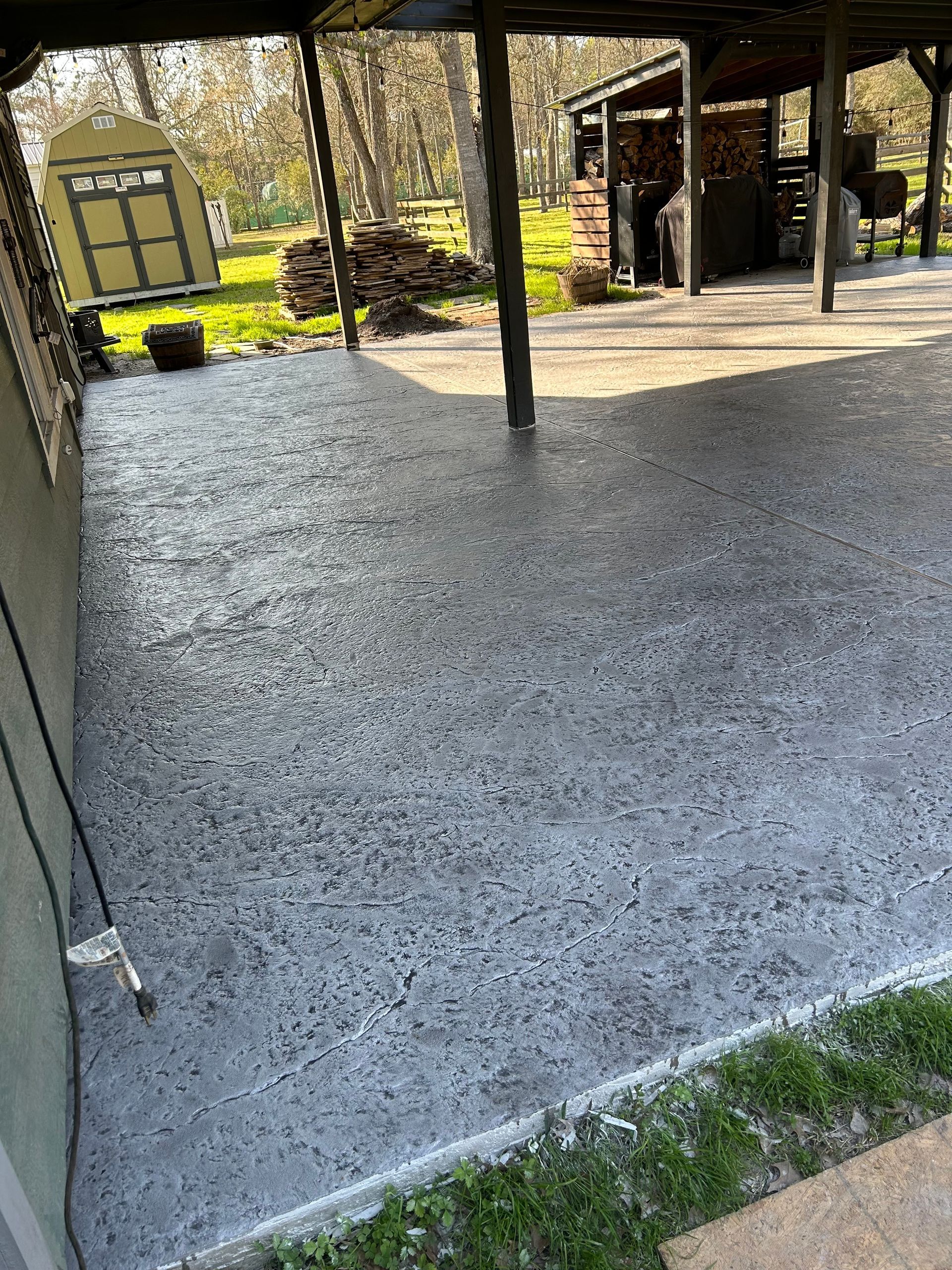 A concrete patio with a covered area and a shed in the background.