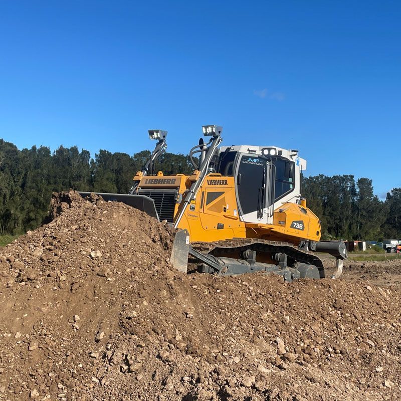 A yellow and white bulldozer is moving dirt in a field