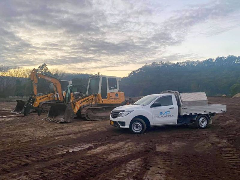 A white truck is parked next to a yellow excavator in a dirt field.