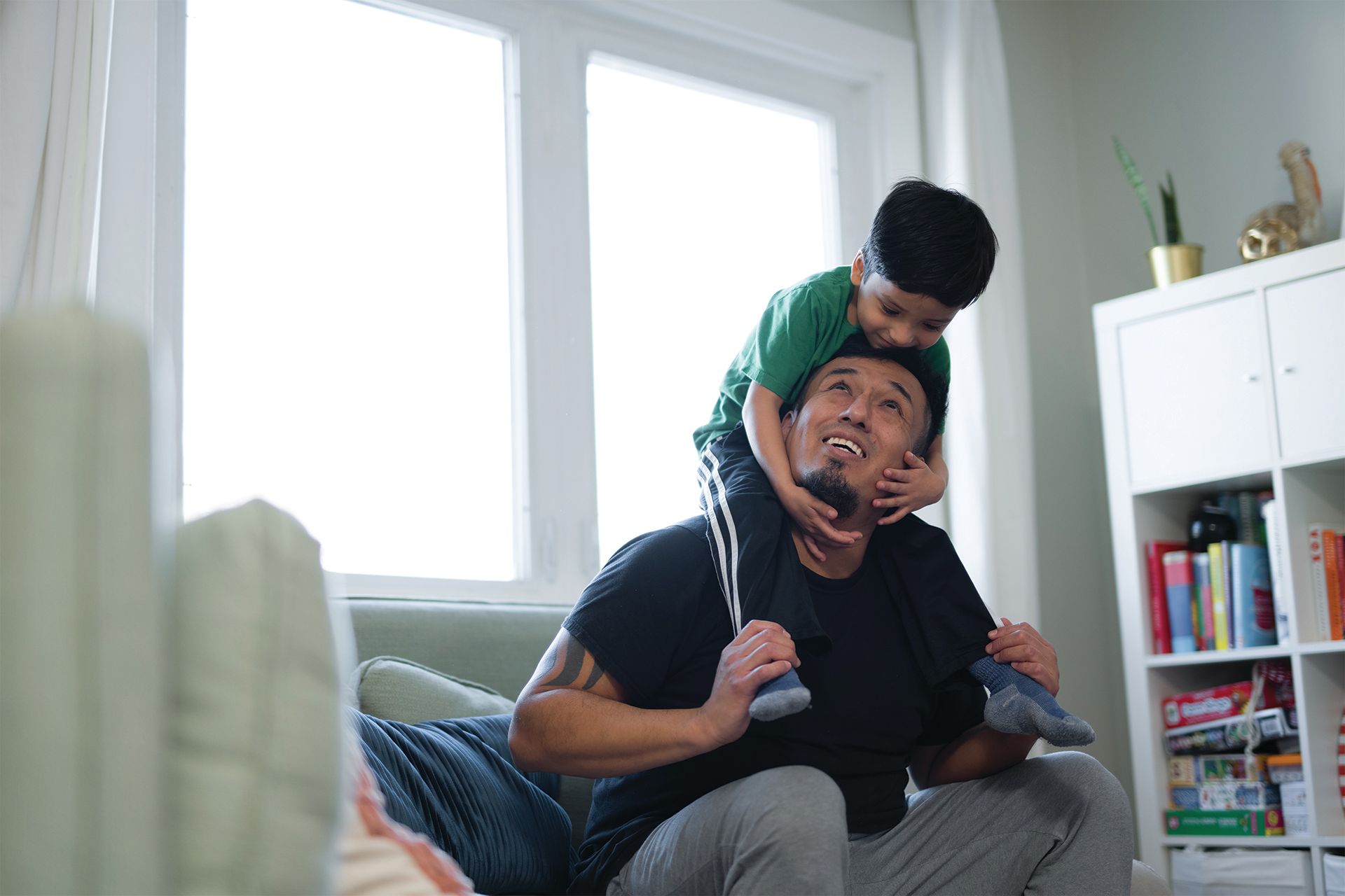 A young boy is sitting on his father's shoulders and they are looking at each other.