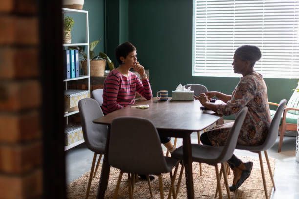 Two women are sitting at a table in a room talking to each other.