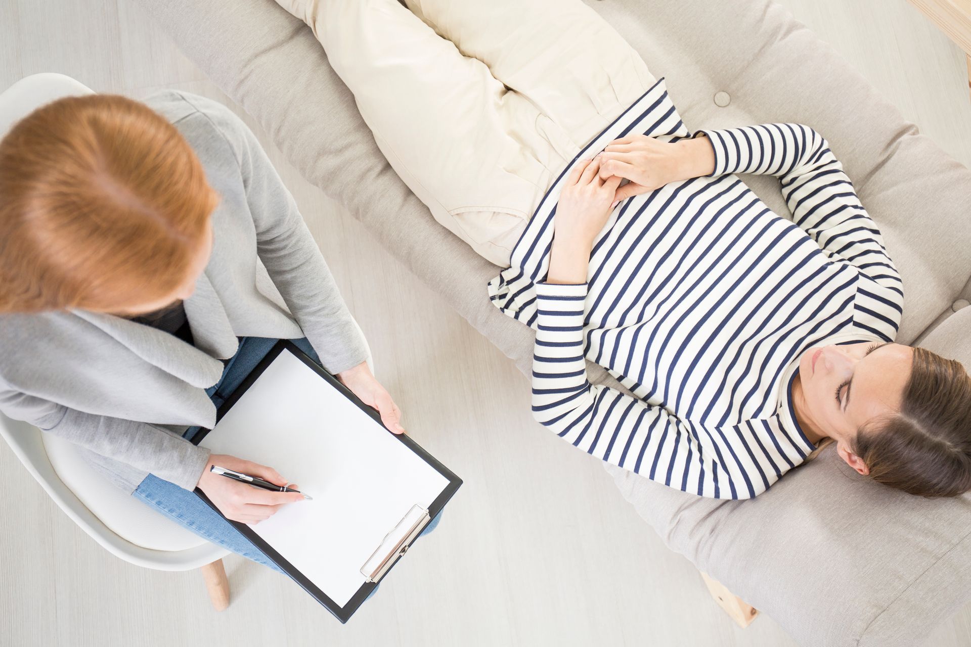 A woman is sitting in a chair talking to a man laying on a couch.