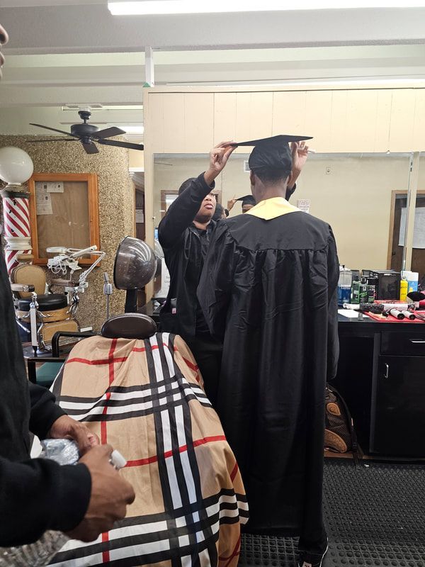 A man in a graduation cap and gown is getting his hair cut