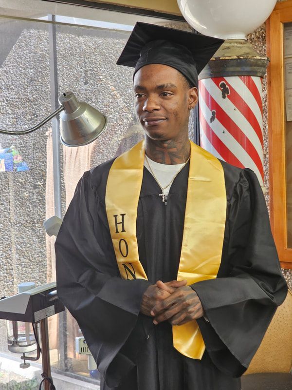 A man in a graduation cap and gown has the letter h on his sash