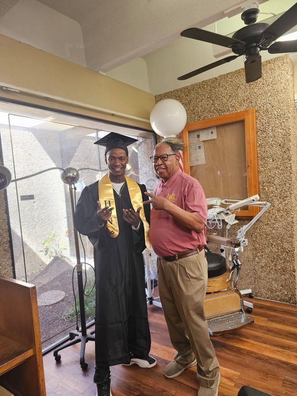 A man in a graduation cap and gown is standing next to a man in a pink shirt.