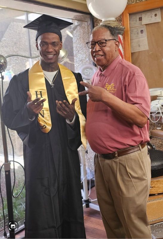 A man in a graduation cap and gown is standing next to a man in a pink shirt.