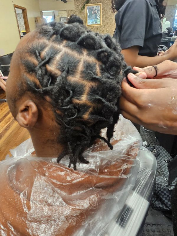 A man with dreadlocks is getting his hair done in a salon