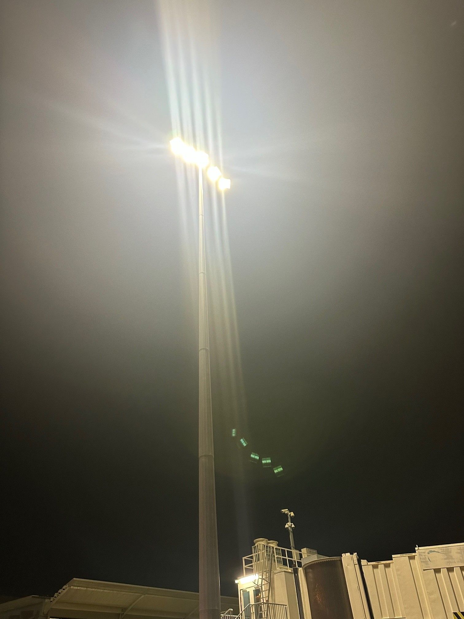 Streetlight glowing at night above a building, with bright glare and lens flare against a dark sky