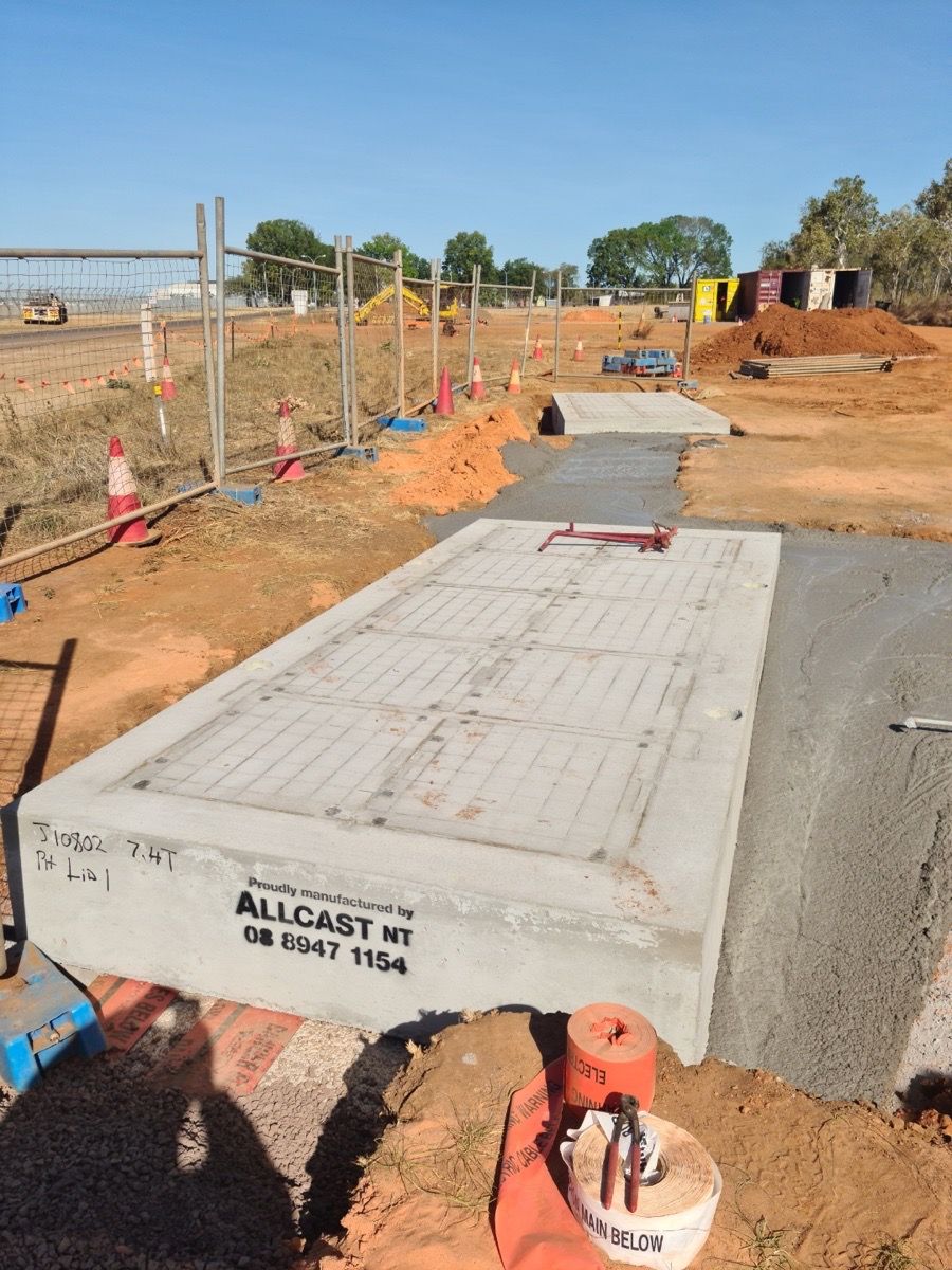 Construction site with a newly poured concrete slab and orange safety fencing along a dirt path