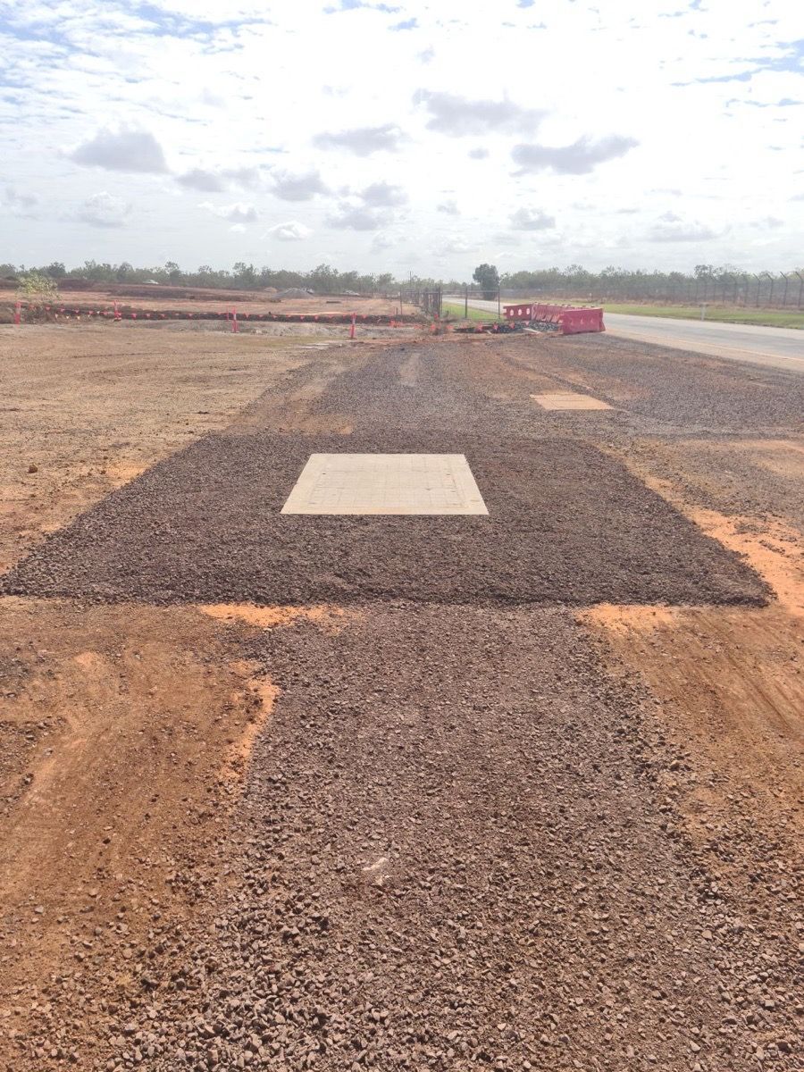 Gravel construction site with a concrete slab in the center under a cloudy sky.