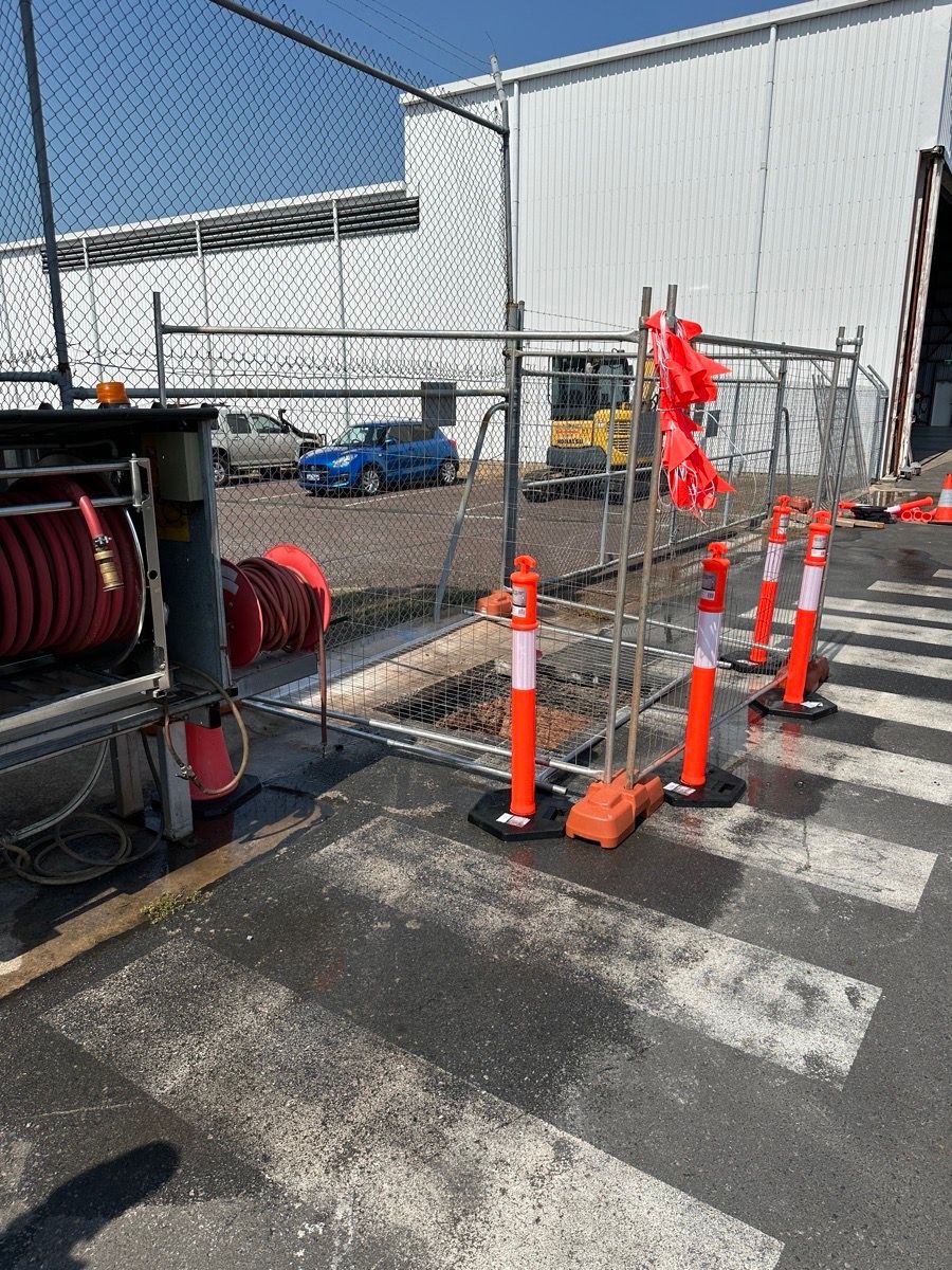 Construction cones and barriers blocking a chain-link gate beside an industrial building.