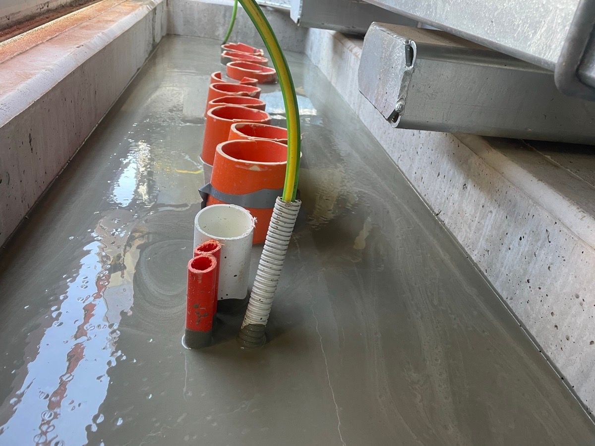 Rows of orange pipes and cables in a wet concrete trench, with water pooling around them