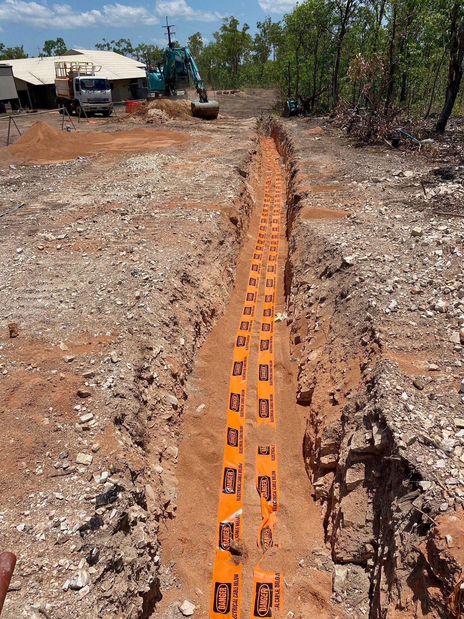 Orange drainage pipe laid in a trench at a construction site, with dirt and equipment in the background
