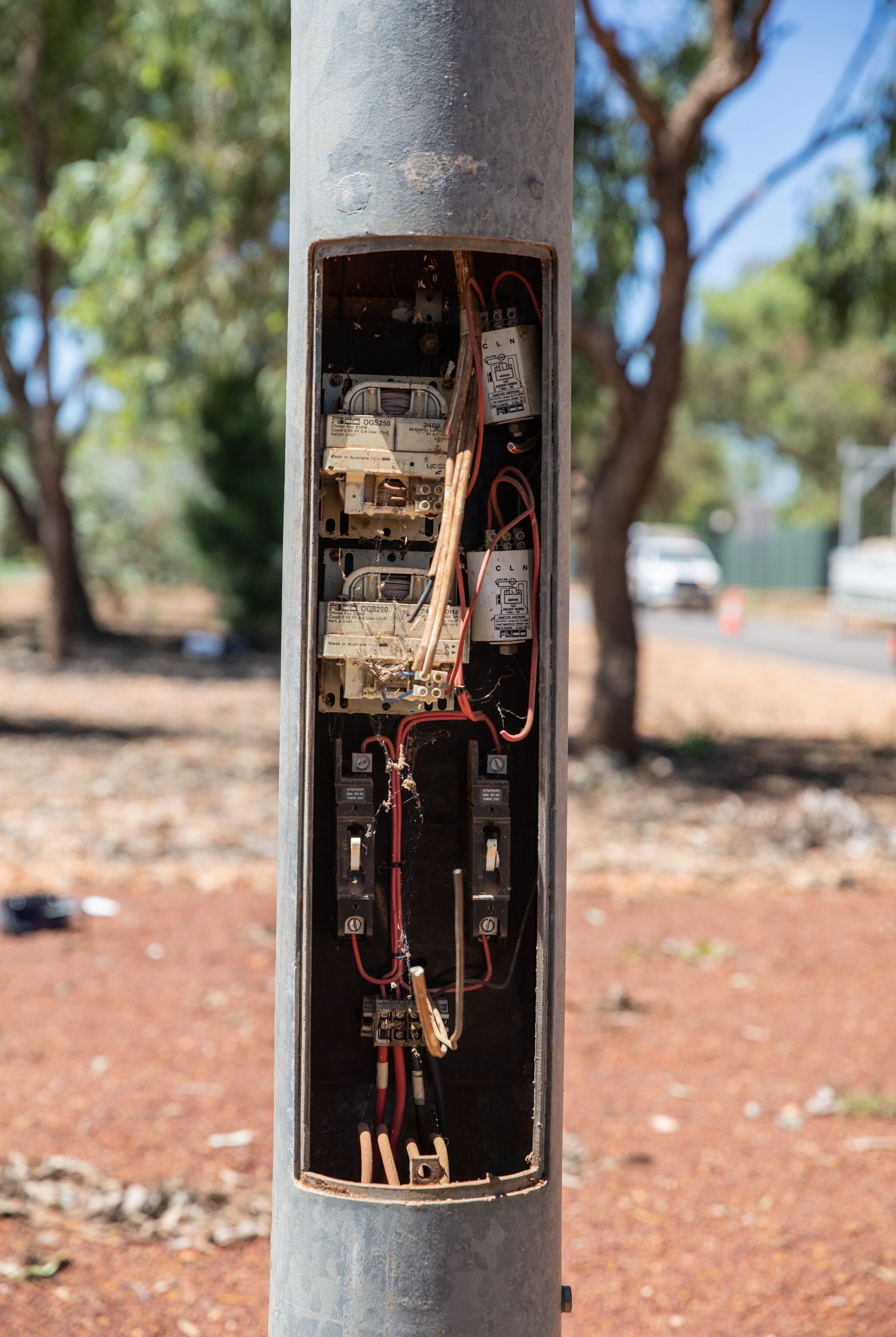 Open electrical control panel inside a metal pole outdoors, with exposed wiring and components