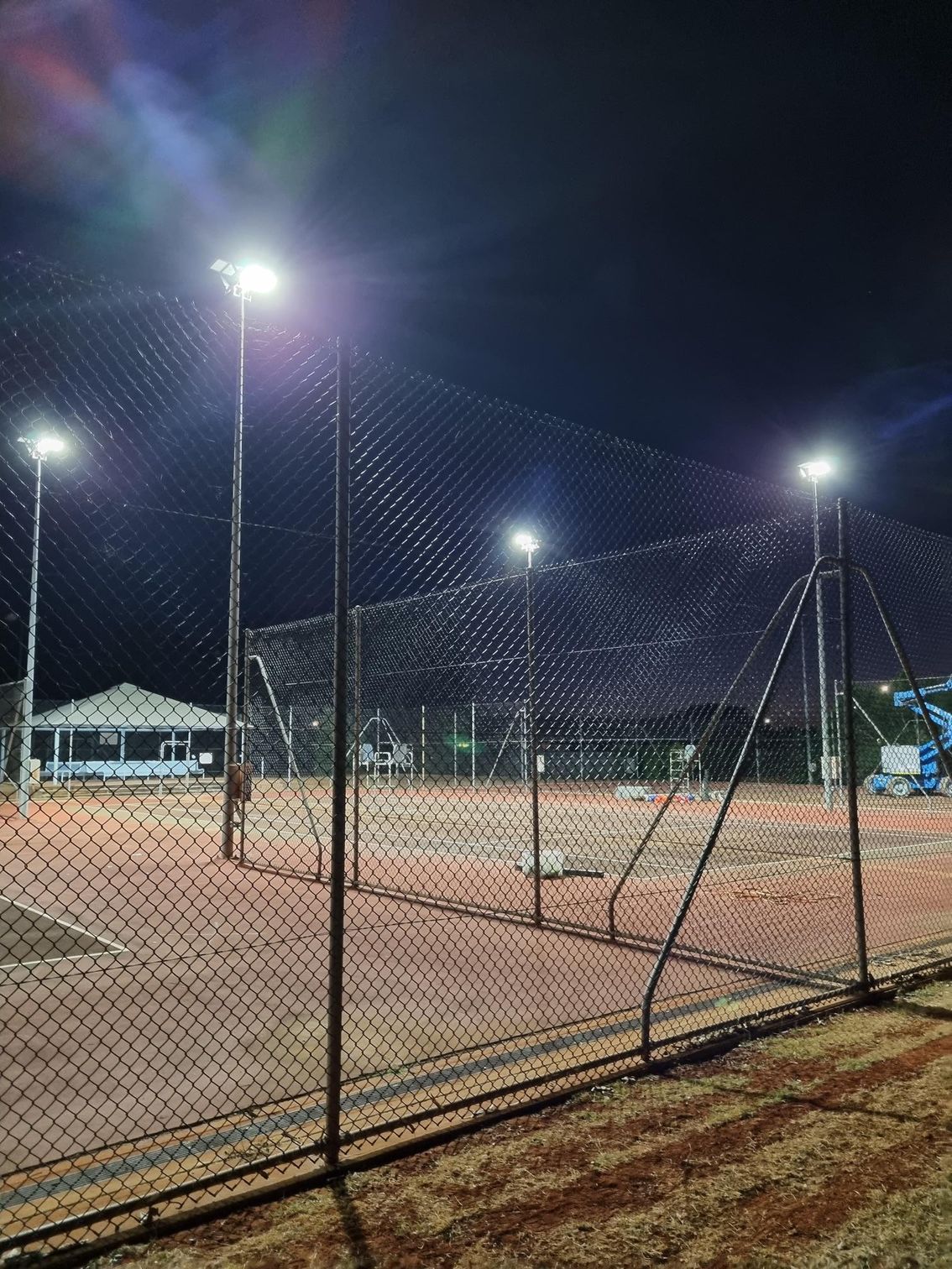 Nighttime view of an empty lit tennis court behind a chain-link fence