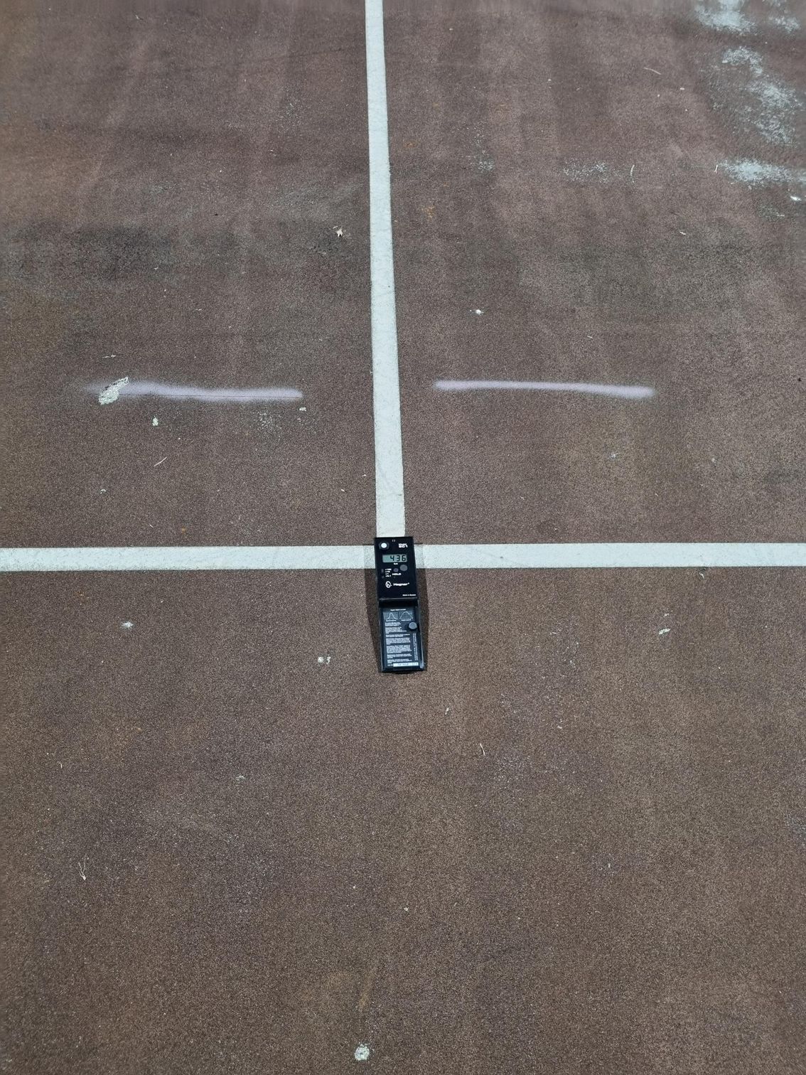 Small black device centered on a brown court floor between white painted lines.