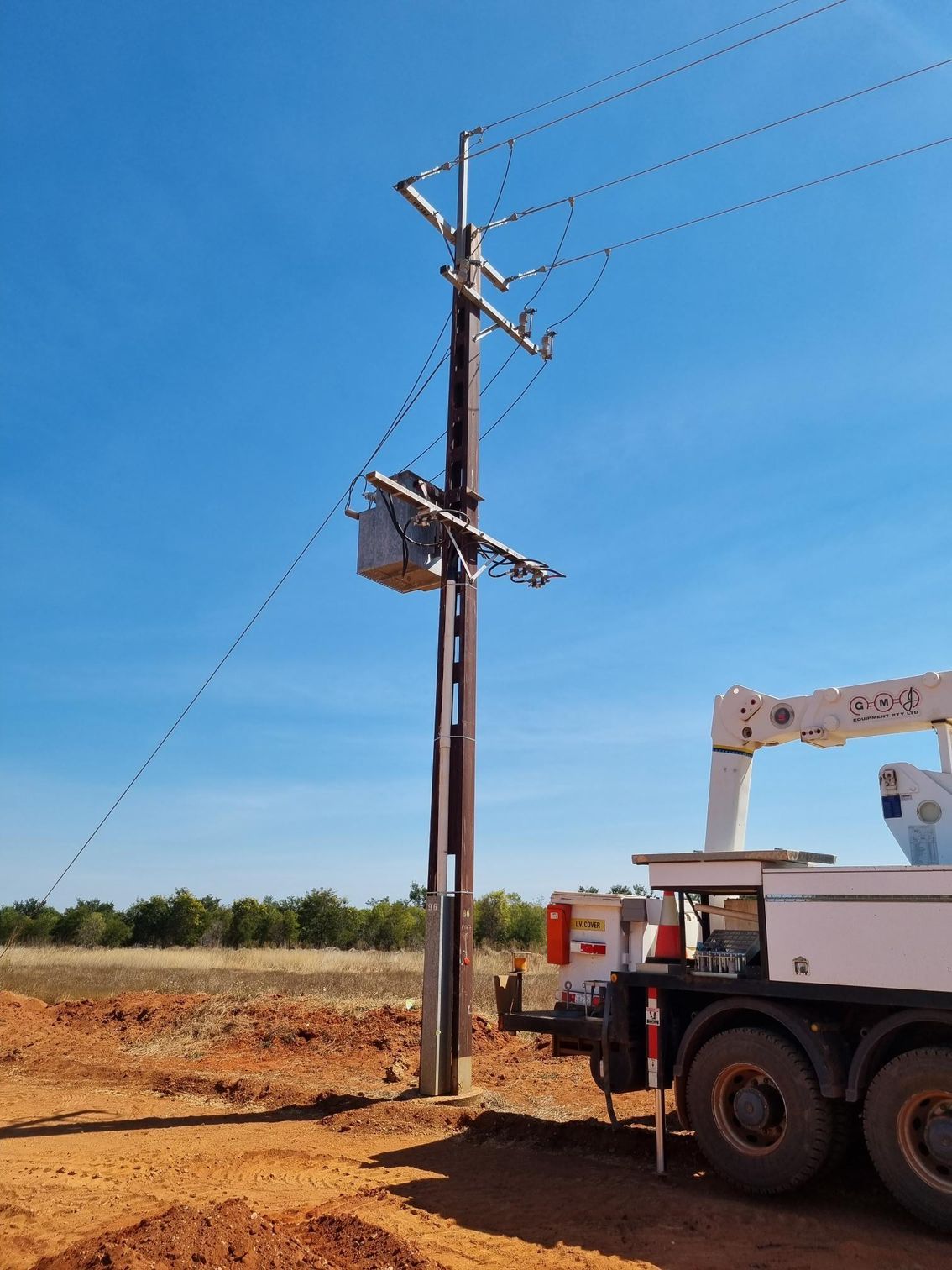 Utility truck beside a power pole on a dirt roadside under a clear blue sky