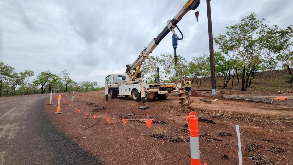 Crane truck lifting materials beside a muddy roadside construction site with orange cones under cloudy skies