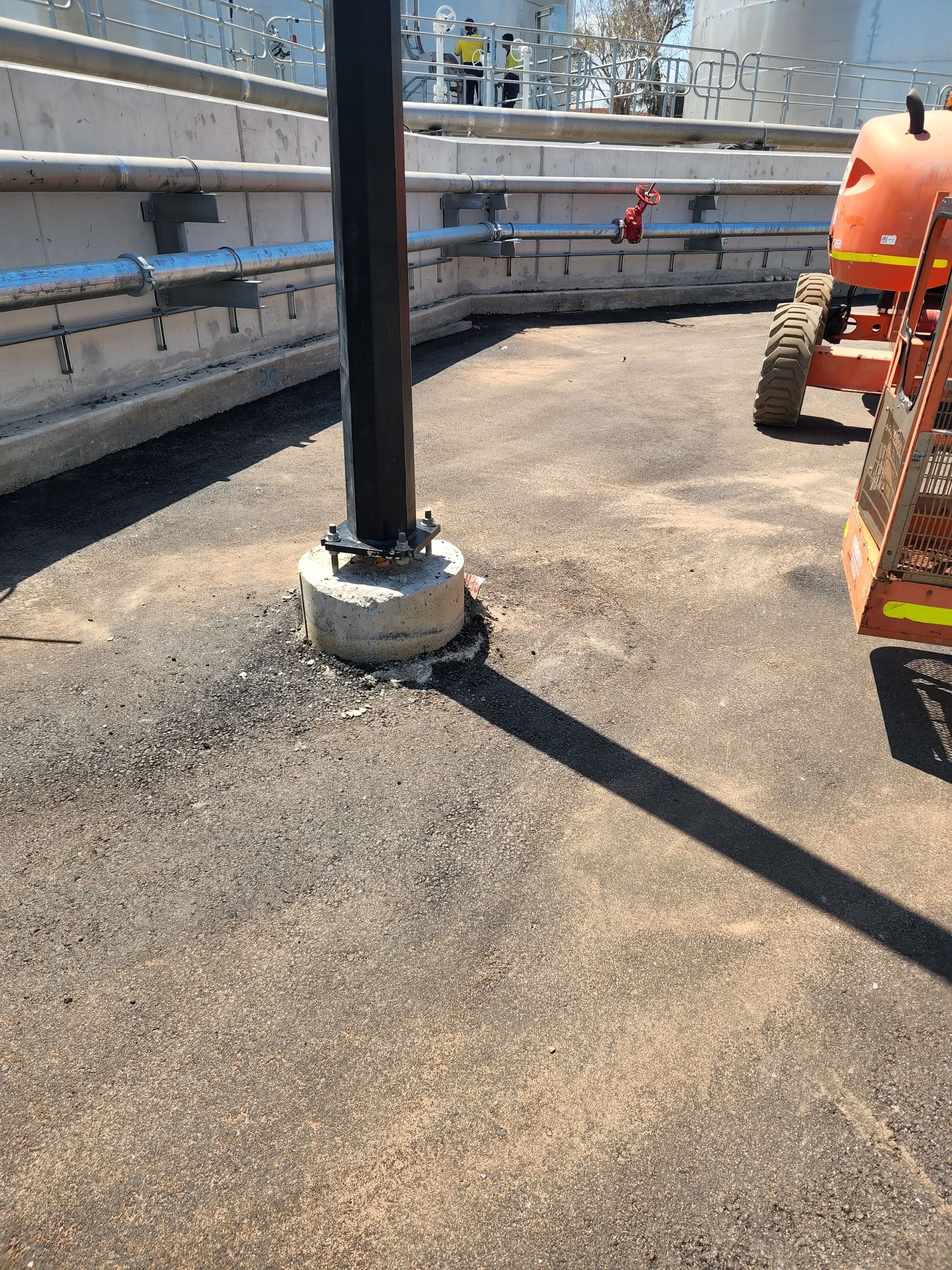 Industrial rooftop with a black pole, gravel surface, railings, and a worker in orange on the right.
