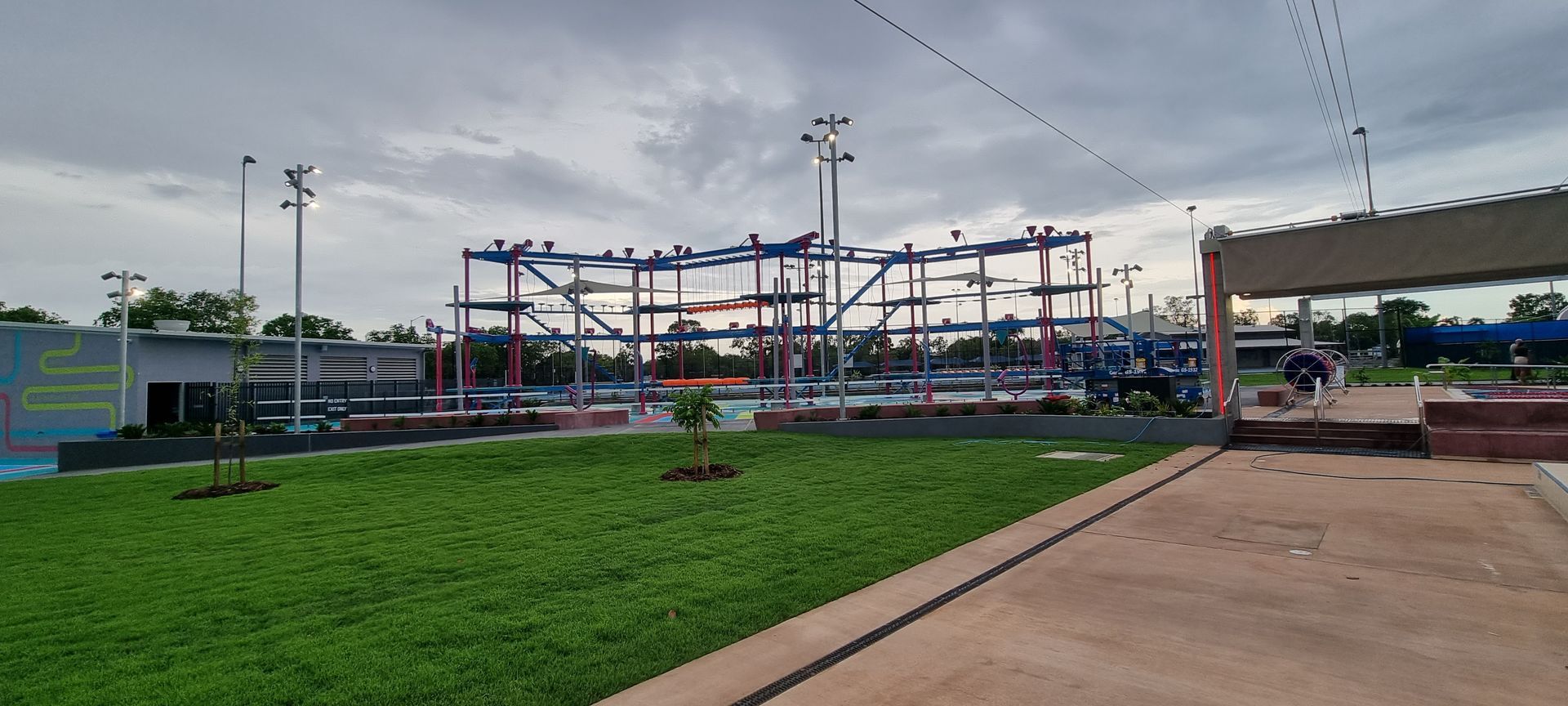 Outdoor park with green lawn, benches, and colorful climbing structures under a cloudy sky
