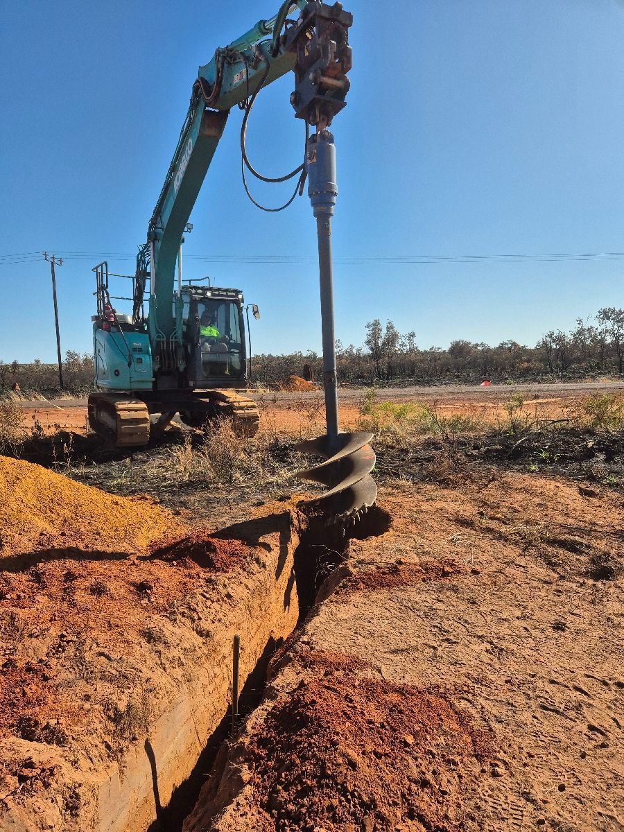 Excavator drilling into dry soil at a construction site under a clear blue sky