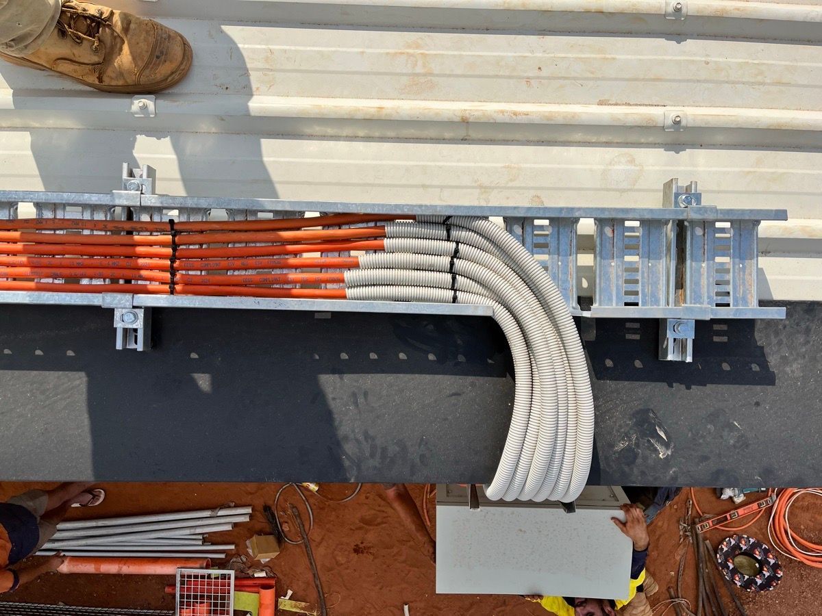 Orange and gray cables bundled along a wall-mounted metal tray in a work area