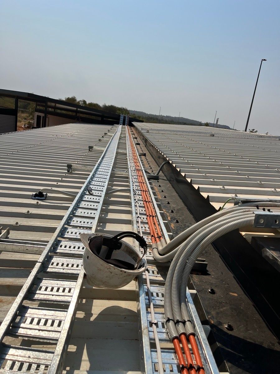 Rooftop cable trays and bundled wires stretching along a long industrial roof under a clear sky