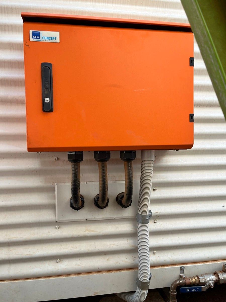 Orange electrical control box with black handle and conduit pipes mounted on a corrugated wall.
