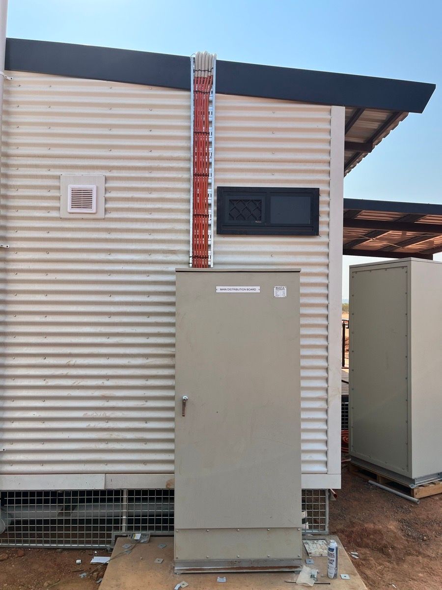 Outdoor utility cabinet beside a corrugated metal building with a red vertical pipe and small window above.