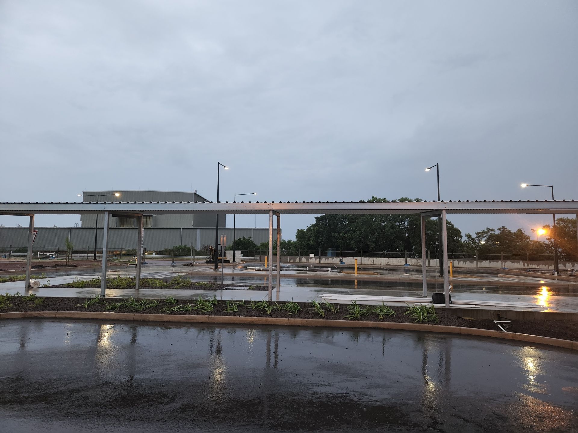 Rainy parking lot with wet pavement, covered walkway, and glowing streetlights at dusk