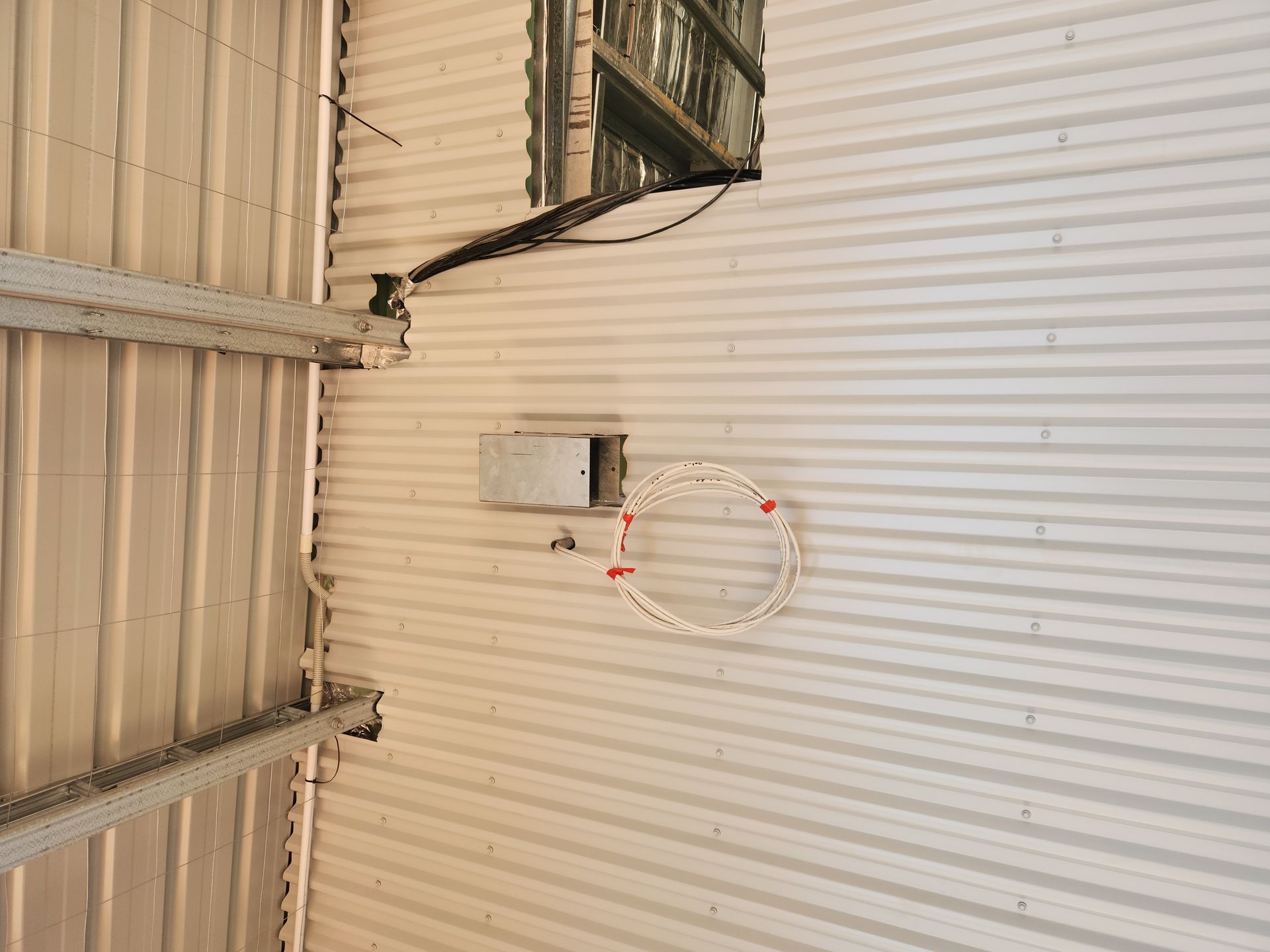 Indoor corrugated metal wall with a small round wall fixture and exposed wiring near the ceiling