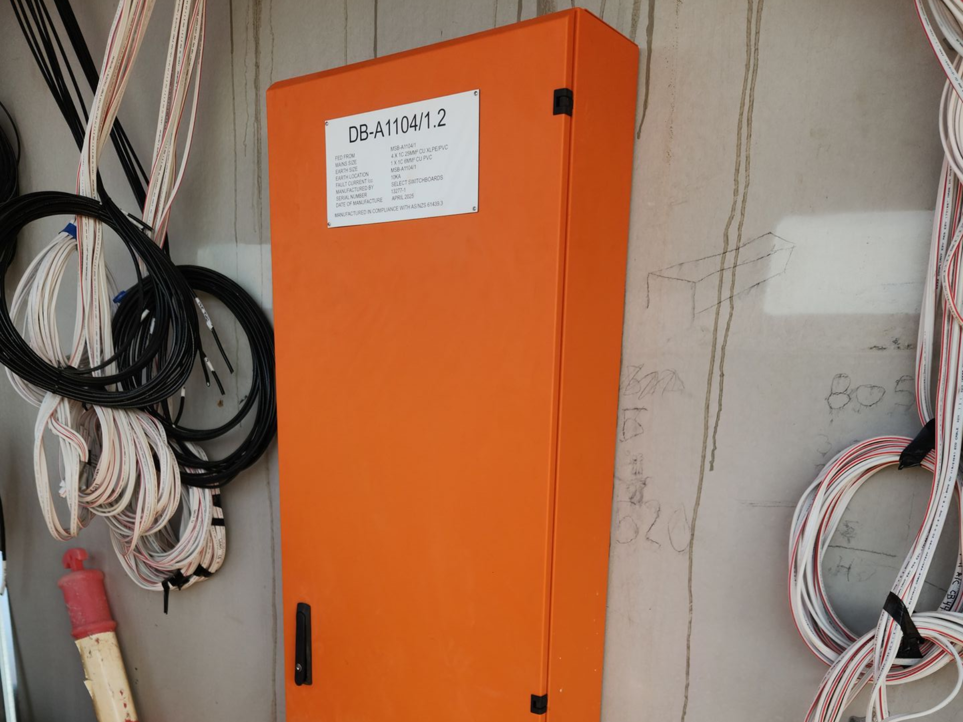 Orange electrical cabinet mounted on a wall, surrounded by coiled cables and wires