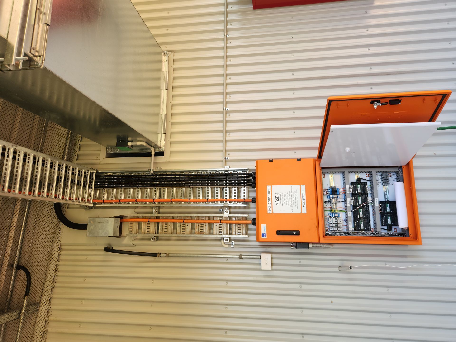 Orange electrical panel with open door and rows of circuit breakers on a wall panel.
