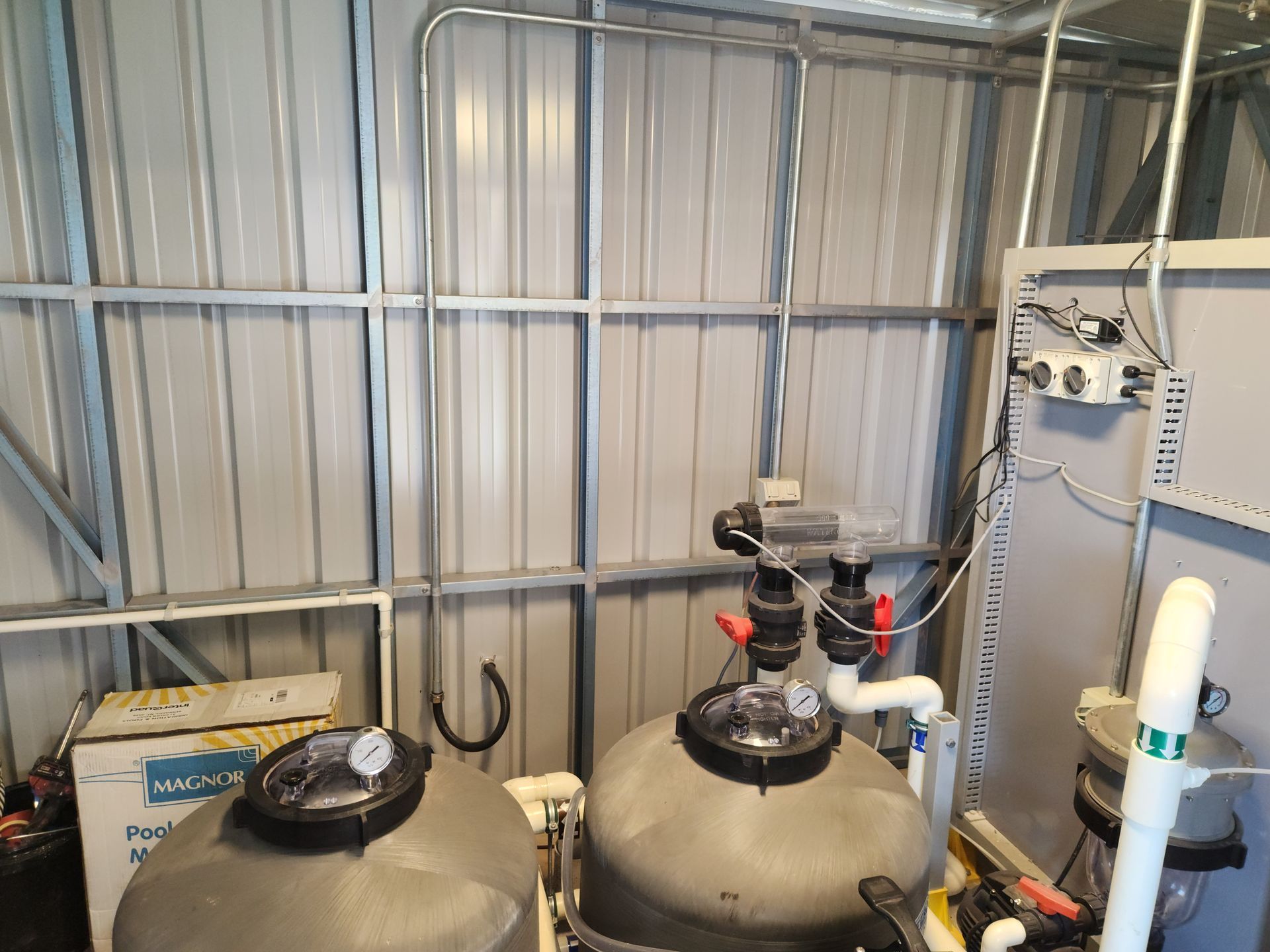 Industrial equipment in a metal shed, with large tanks, pipes, and a wall-mounted control panel.