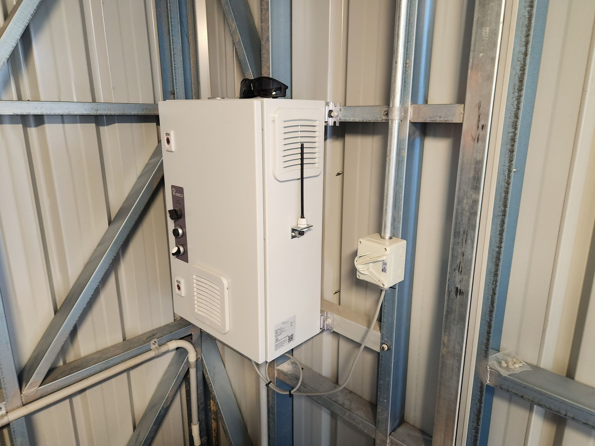 White electrical control box mounted on a metal wall in a utility room with exposed framing.