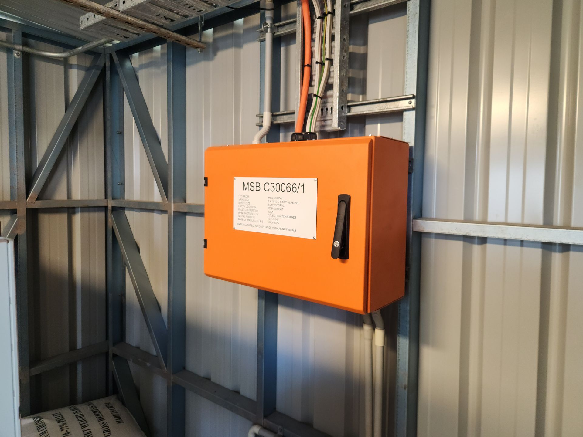 Orange electrical control box mounted on a corrugated metal wall in an industrial interior