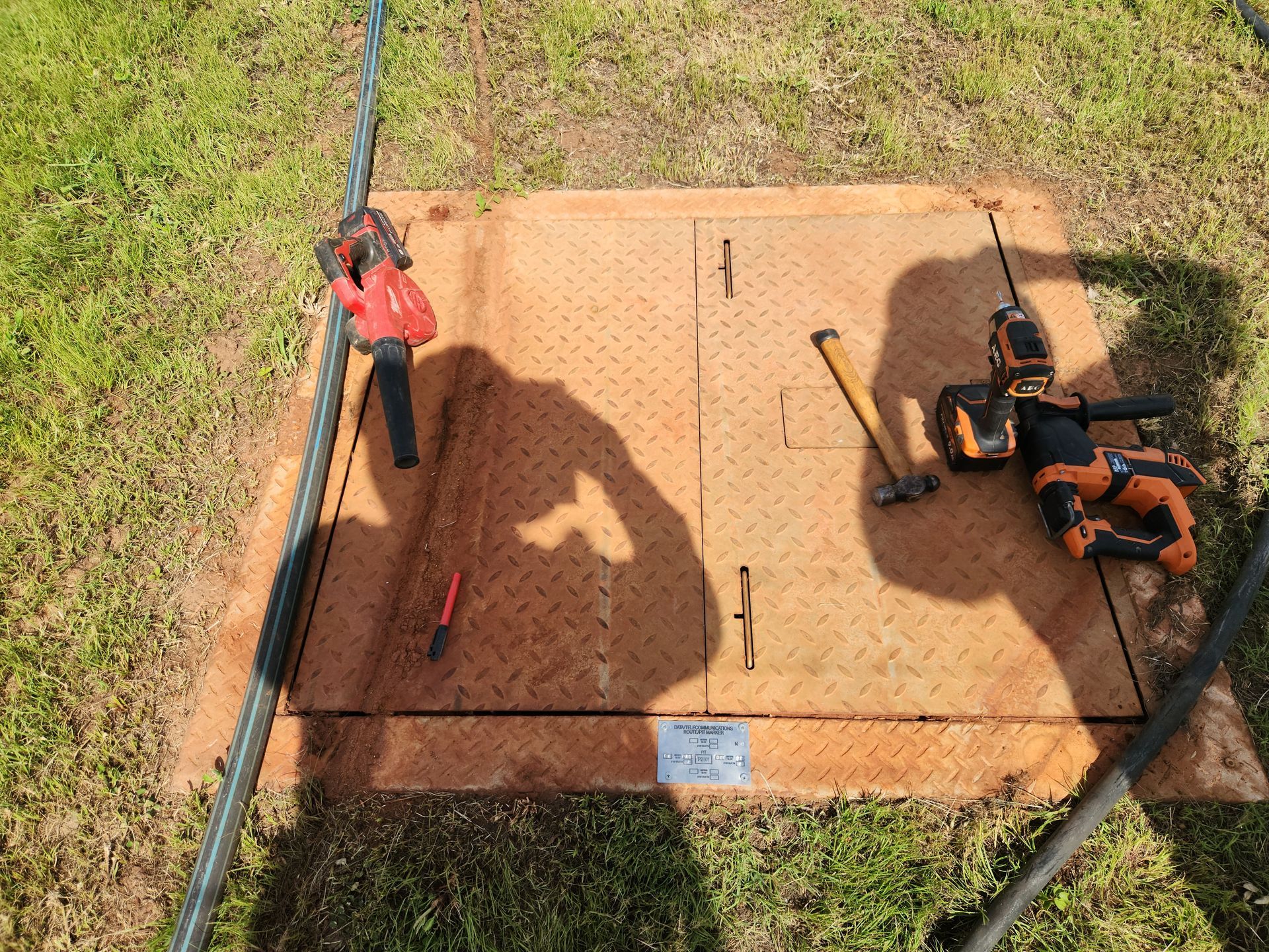 Orange lawn mower and red trimmer on a concrete pad beside a grassy yard, viewed from above.