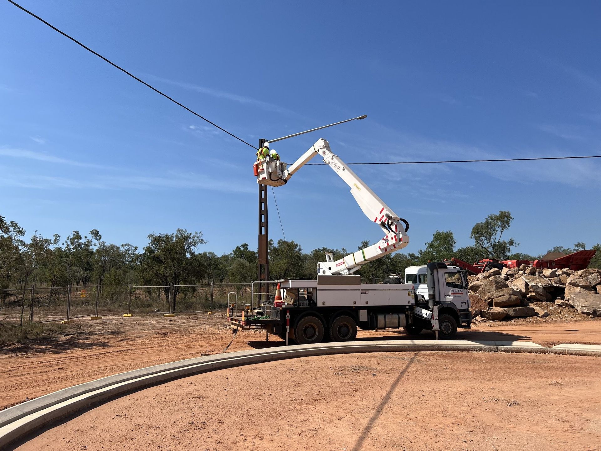 Bucket truck repairing overhead power lines on a dirt road in a rural area