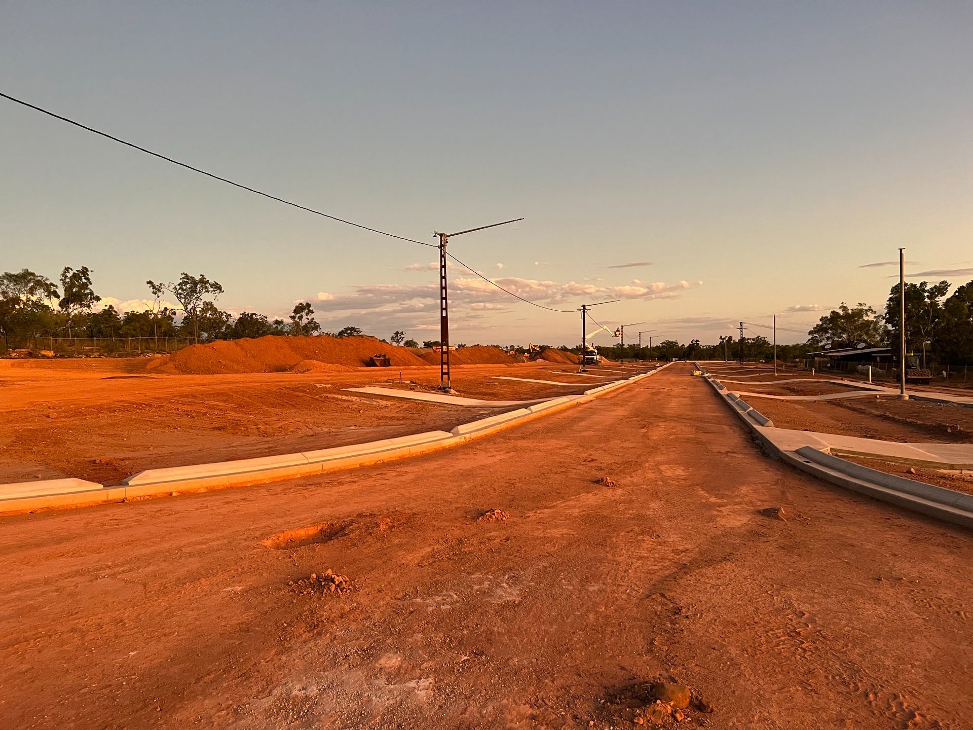 Empty dirt road at sunset with streetlights and sparse trees under a clear sky