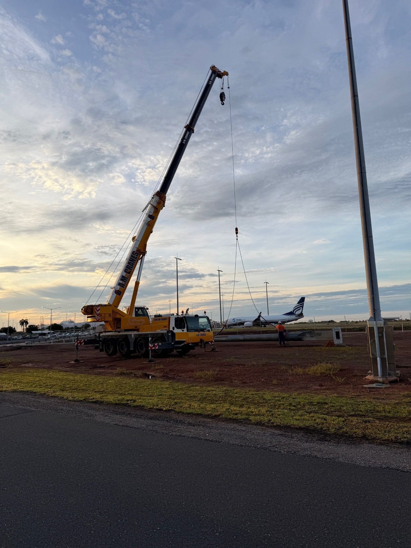 Yellow crane lifting near parked airplanes at dusk on an airport tarmac