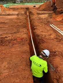 Worker in neon safety shirt aligns a long pipe in a muddy trench at a construction site