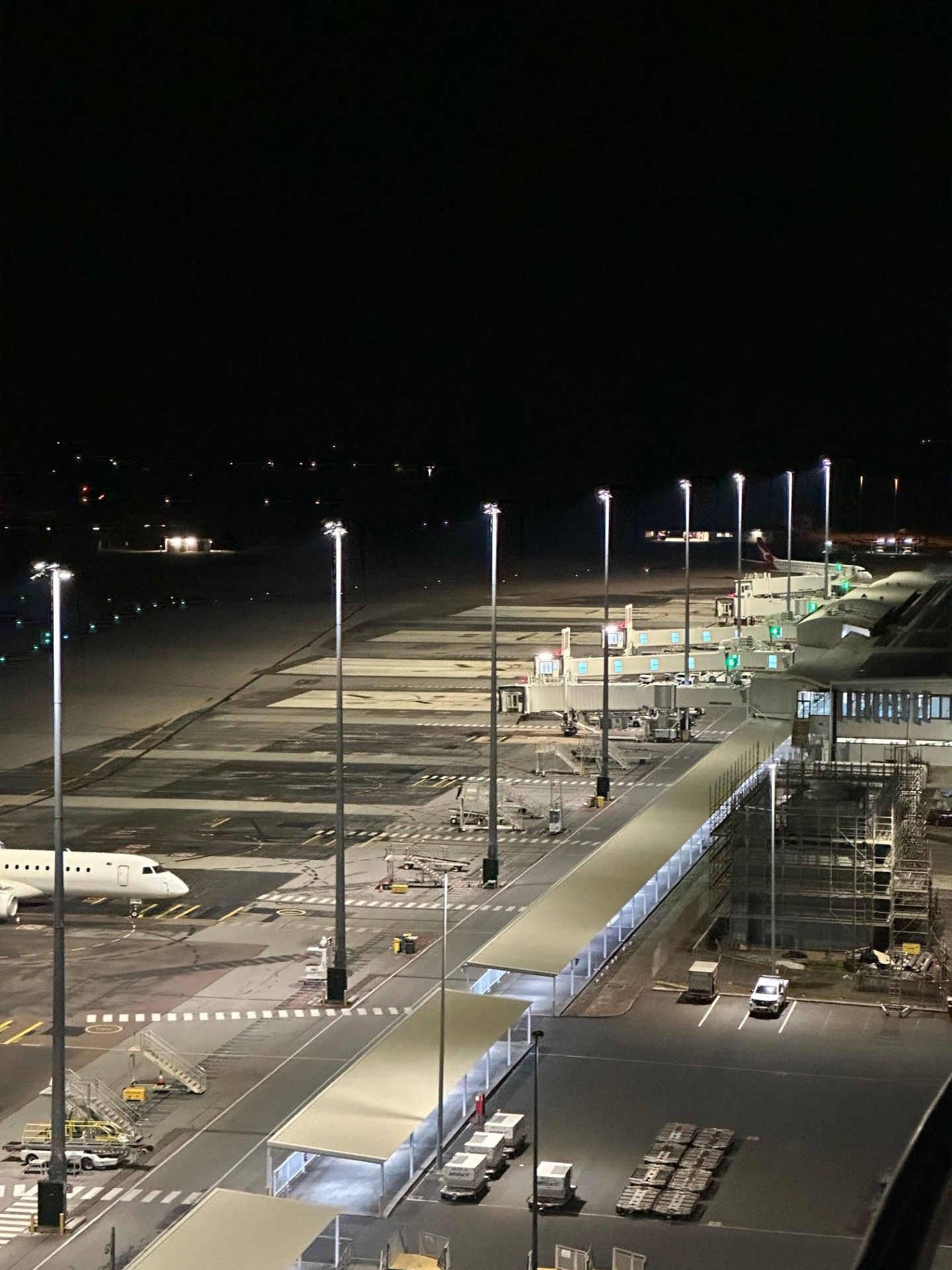 Nighttime airport tarmac with parked airplanes, bright floodlights, and a long covered walkway.