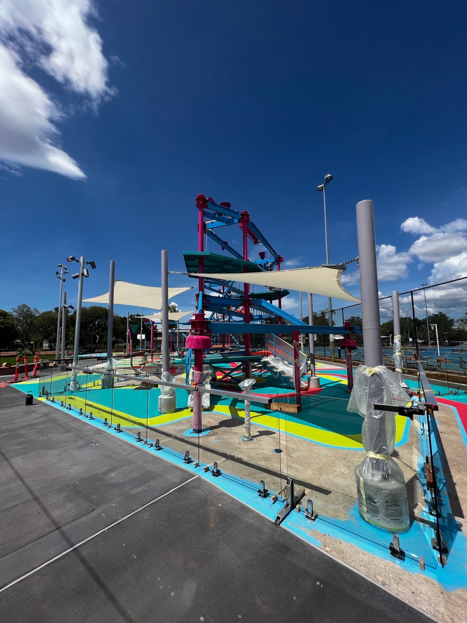 Outdoor playground with colorful climbing structures, slides, and shade sails under a blue sky