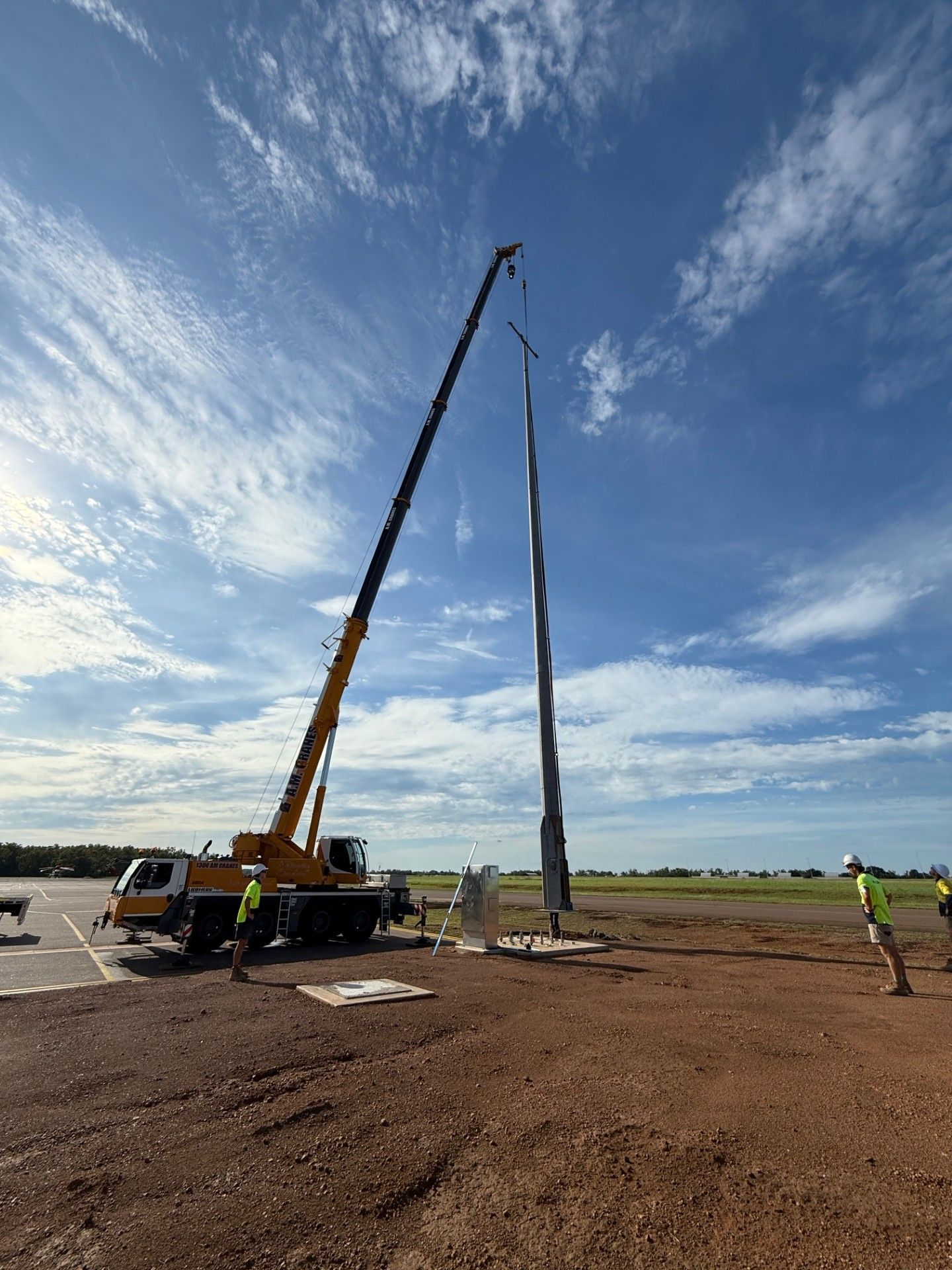 Crane lifting a tall utility pole at a construction site under a blue sky