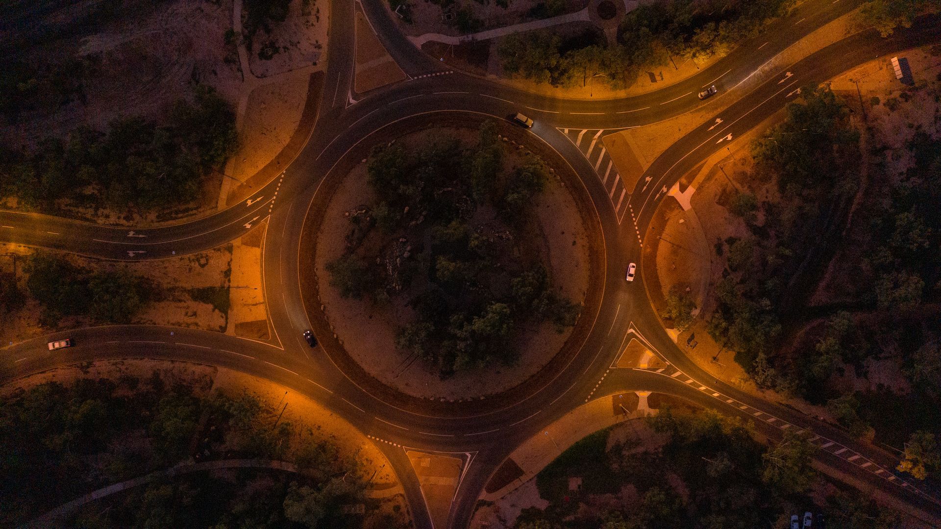 Aerial view of a dark circular roundabout with warm orange streetlights and surrounding roads at night